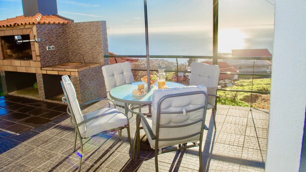 Eine Terrasse im Freien mit einem Stein-Barbecue, einem Glastisch und weißen Sitzgelegenheiten.