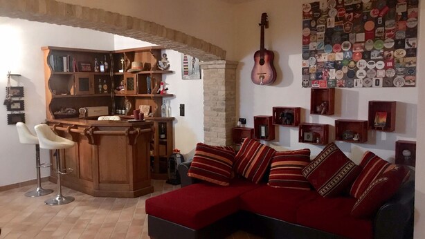 A cozy living room with a red sofa, a wooden bar area, and a guitar wall art. - Modern open space tavern, with shared garden use (Numana)