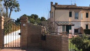 A gated entrance with a brick wall and metal gate, leading to a building with a tiled roof and a small porch. - Modern open space tavern, with shared garden use (Numana)