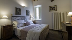Un dormitorio con una cama, dos mesitas de noche con lámparas, un radiador y dos cuadros en la pared.