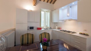 Una cocina moderna con armarios blancos, una estufa a gas y un ventanal. Hay una mesa de comedor con sillas y un jarrón de flores.
