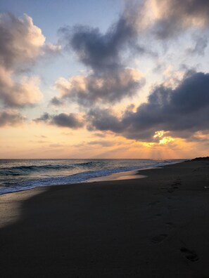 Ein Strand mit Sonnenuntergang, Wellen und Fußspuren im Sand.
