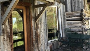 Ein rustikales Holzhäuschen mit Veranda, einem Esstisch mit Stühlen und einem Fenster mit Blick auf eine grüne Landschaft.