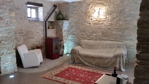 Une pièce aux murs de pierre, avec un radiateur rouge, une chaise blanche, un canapé recouvert d’un tissu et un tapis rouge à motifs.