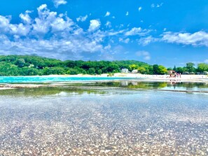 A beach with clear water, a sandy shore, and a forested hill in the background. - Cozy Cedar Cottage Just Off Scenic M22 by Lower Herring Lake (Frankfort)