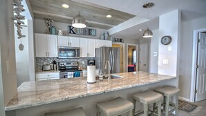 Una cocina con una isla grande, armarios blancos, electrodomésticos de acero inoxidable e iluminación colgante.
