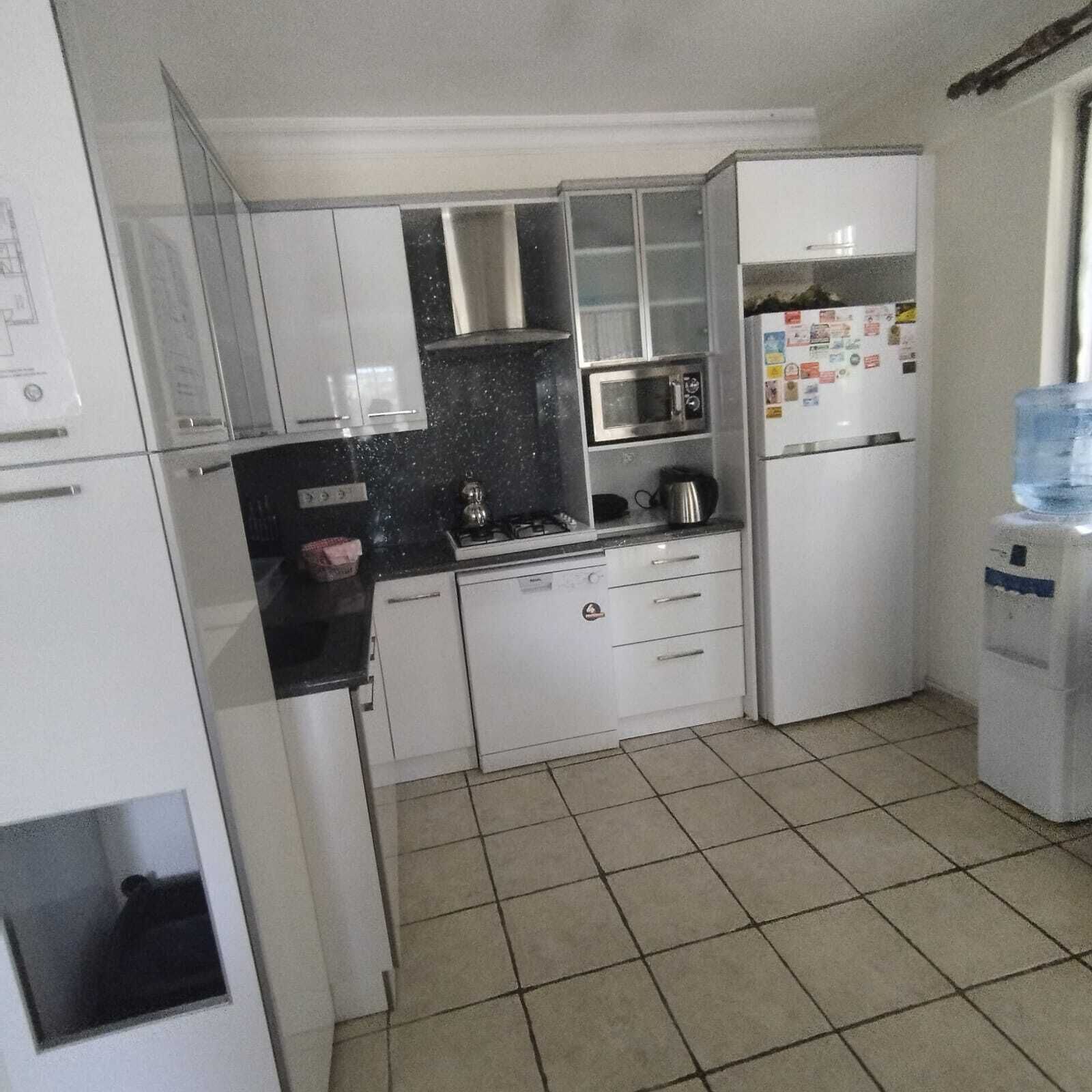 Uma cozinha compacta com armários brancos, micro-ondas, geladeira e dispenser de água.