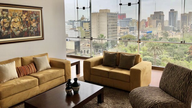 A living room with two sofas, a coffee table, and a large window offering a city view. - Kennedy Park Miraflores apartment (Miraflores)
