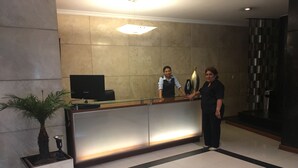 A reception desk with a flat-screen TV, a potted plant, and a modern wall design. - Kennedy Park Miraflores apartment (Miraflores)