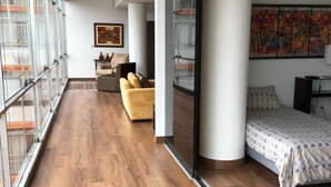 A modern hotel room with a large sliding glass door, a bed with a patterned bedspread, a sofa, and a painting on the wall. - Kennedy Park Miraflores apartment (Miraflores)