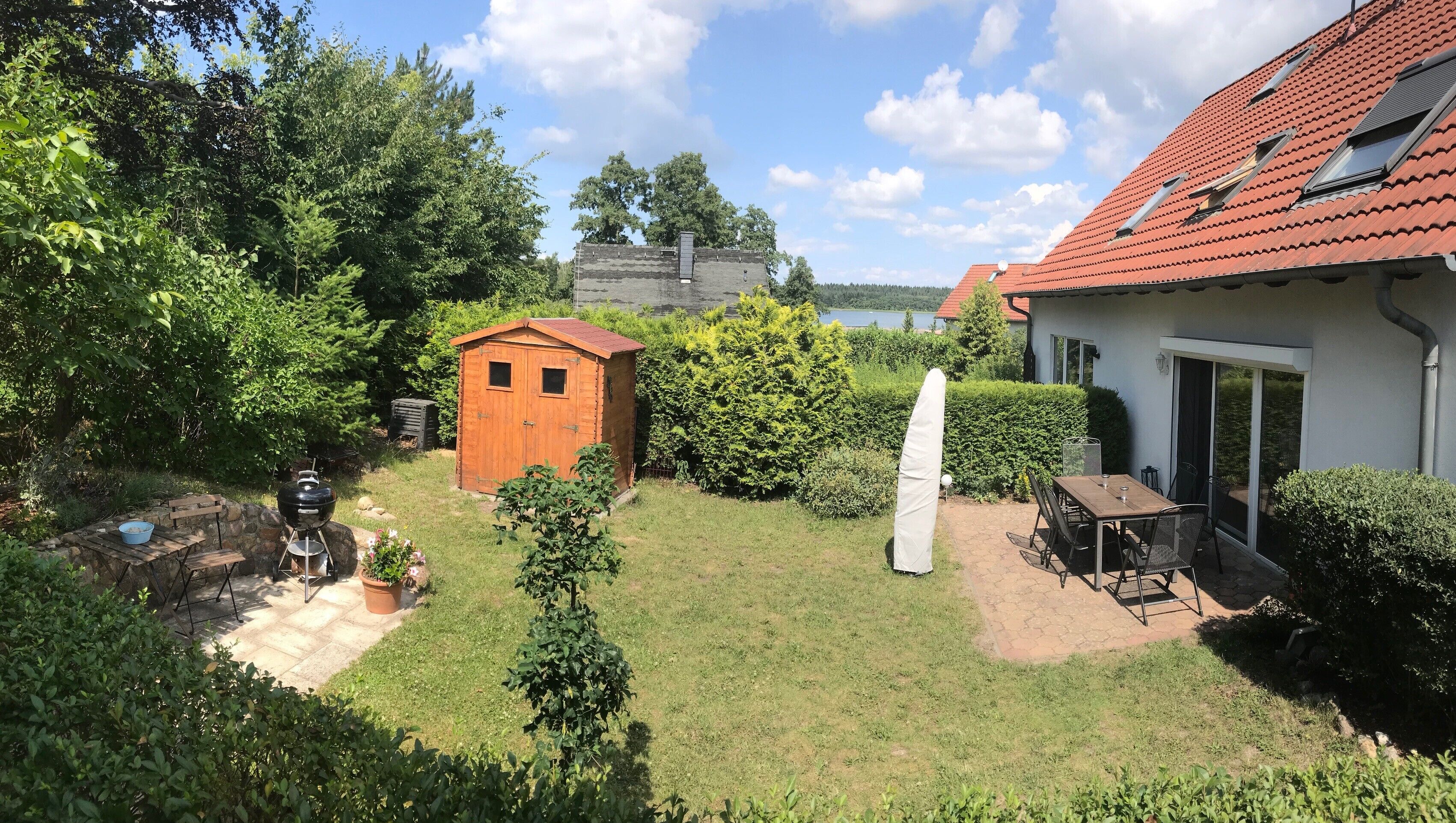 A backyard with a wooden shed, a barbecue grill, and a dining area with a table and chairs.