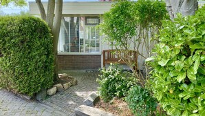 A garden with a brick pathway, a wooden bench, and a variety of green plants. - Cozy bungalow in rural area near beautiful dunes, beach and sea. (Schoorldam)