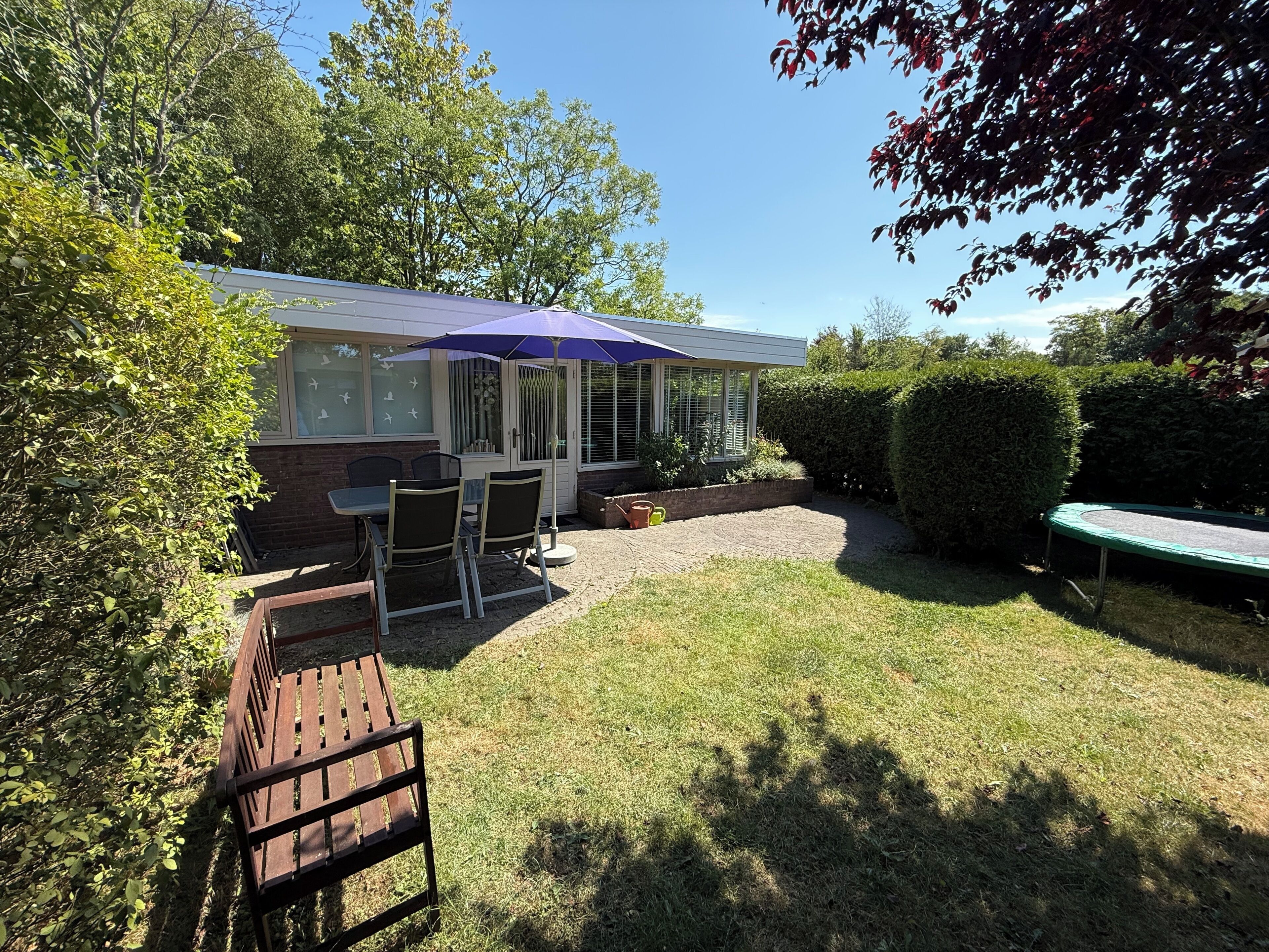Een huis met een terras, een tafel met stoelen en een trampoline.