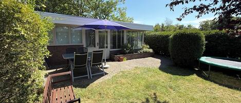 Een huis met een terras, een tafel met stoelen en een trampoline.