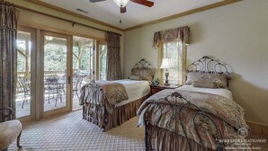 Un dormitorio con dos camas, un ventilador de techo, una ventana con cortinas y vistas al exterior.