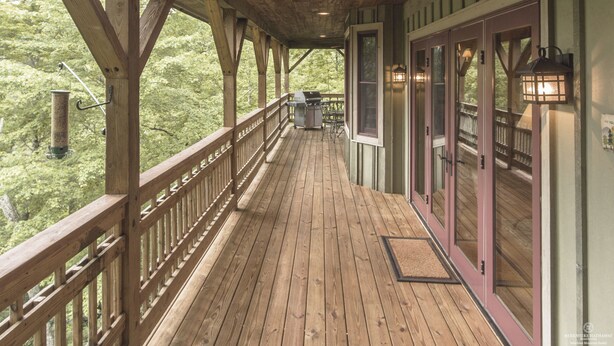 Una terraza de madera con barandilla, una parrilla y una puerta con paneles de vidrio.