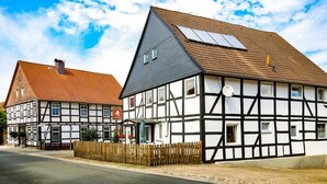 A traditional half-timbered house with a sloped roof, a visible chimney, and a small garden area with a wooden fence. - Historic coach house is looking forward to two and four-legged friends (Coppenbrügge)