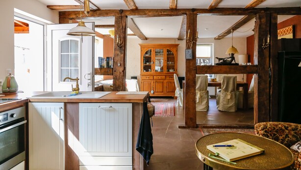 A kitchen with a wooden island, a dining area with a table and chairs, and a living room with a sofa and a small table. - Historic coach house is looking forward to two and four-legged friends (Coppenbrügge)