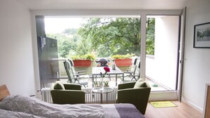 Un dormitorio con una cama grande, un balcón con asientos y una mesa, y vistas a zonas verdes.