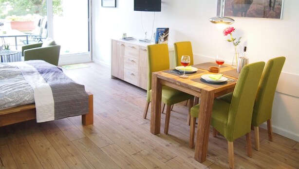 Una habitación moderna con una cama, una mesa de comedor con sillas, un televisor y obras de arte en la pared.
