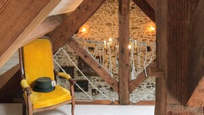 Un dormitorio rústico en el ático con una silla amarilla, un adorno de pared y una pared de piedra con cuerda de ratán.