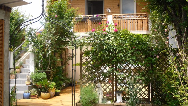 Un balcón de madera con barandilla de madera, plantas en macetas y un suelo de madera.