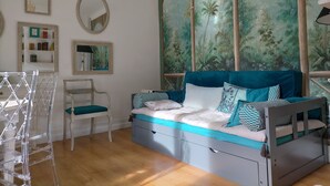 Un dormitorio con una cama, una silla, una estantería y un amplio ventanal con un mural de un bosque.