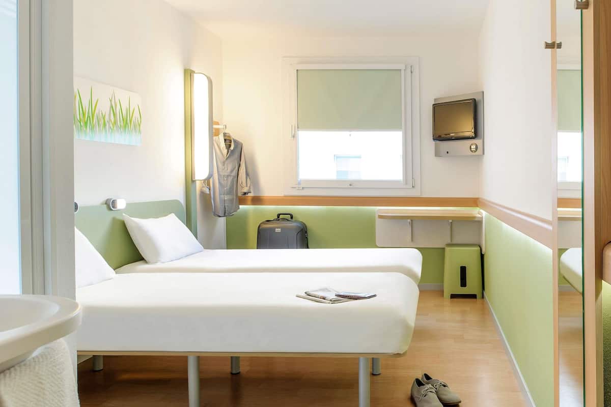 Ein Hotelzimmer mit zwei Betten, einem Schreibtisch, einem Fernseher und einem Koffer.