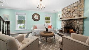 A living room with a stone fireplace, a chandelier, and a white sofa. - East Hampton Luxury: Heated Pool, Hot Tub and Expansive Yard with 6 Bedrooms (East Hampton)