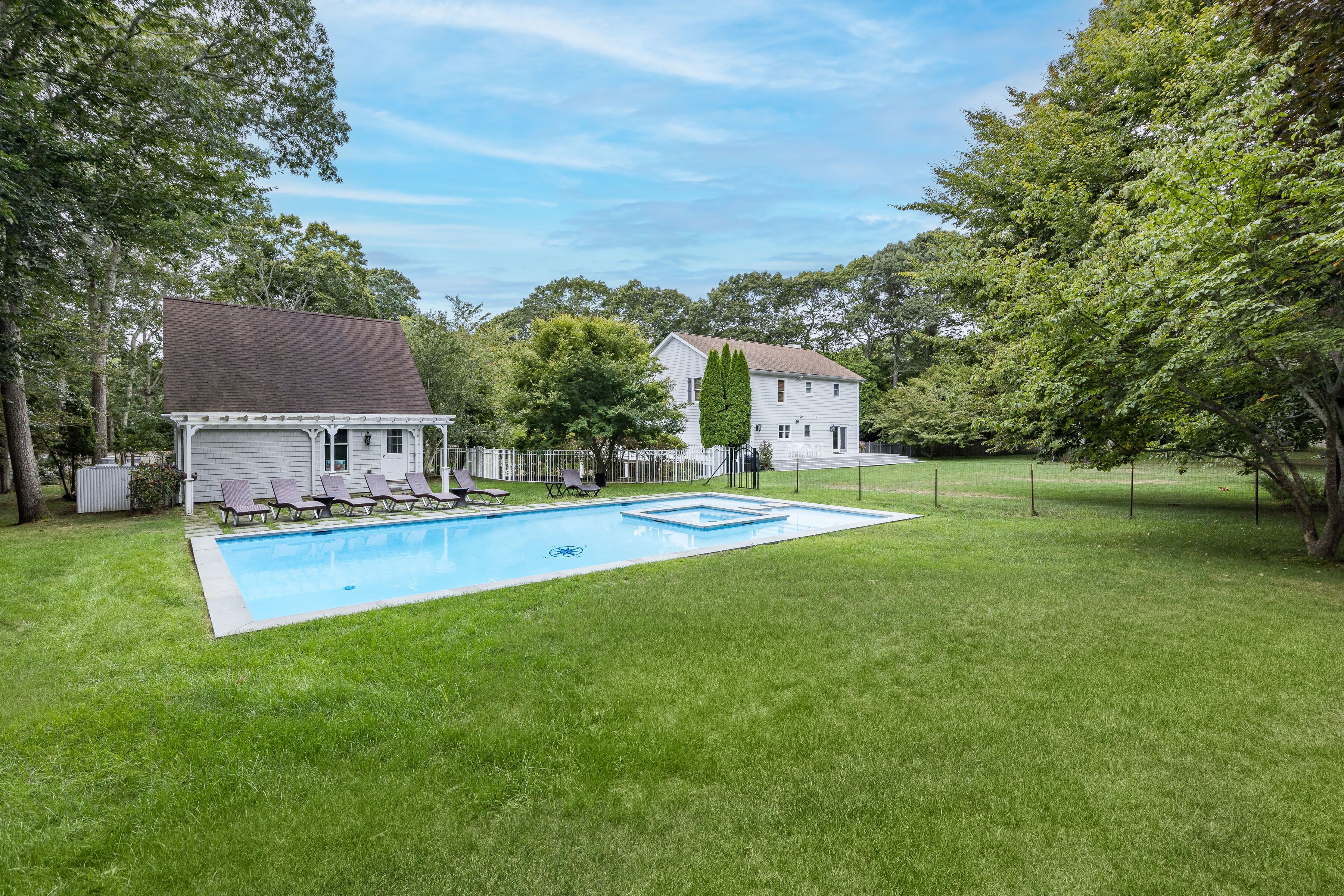 A backyard with a swimming pool, a covered garage, and a white house surrounded by trees.