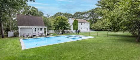 A backyard with a swimming pool, a covered garage, and a white house surrounded by trees.