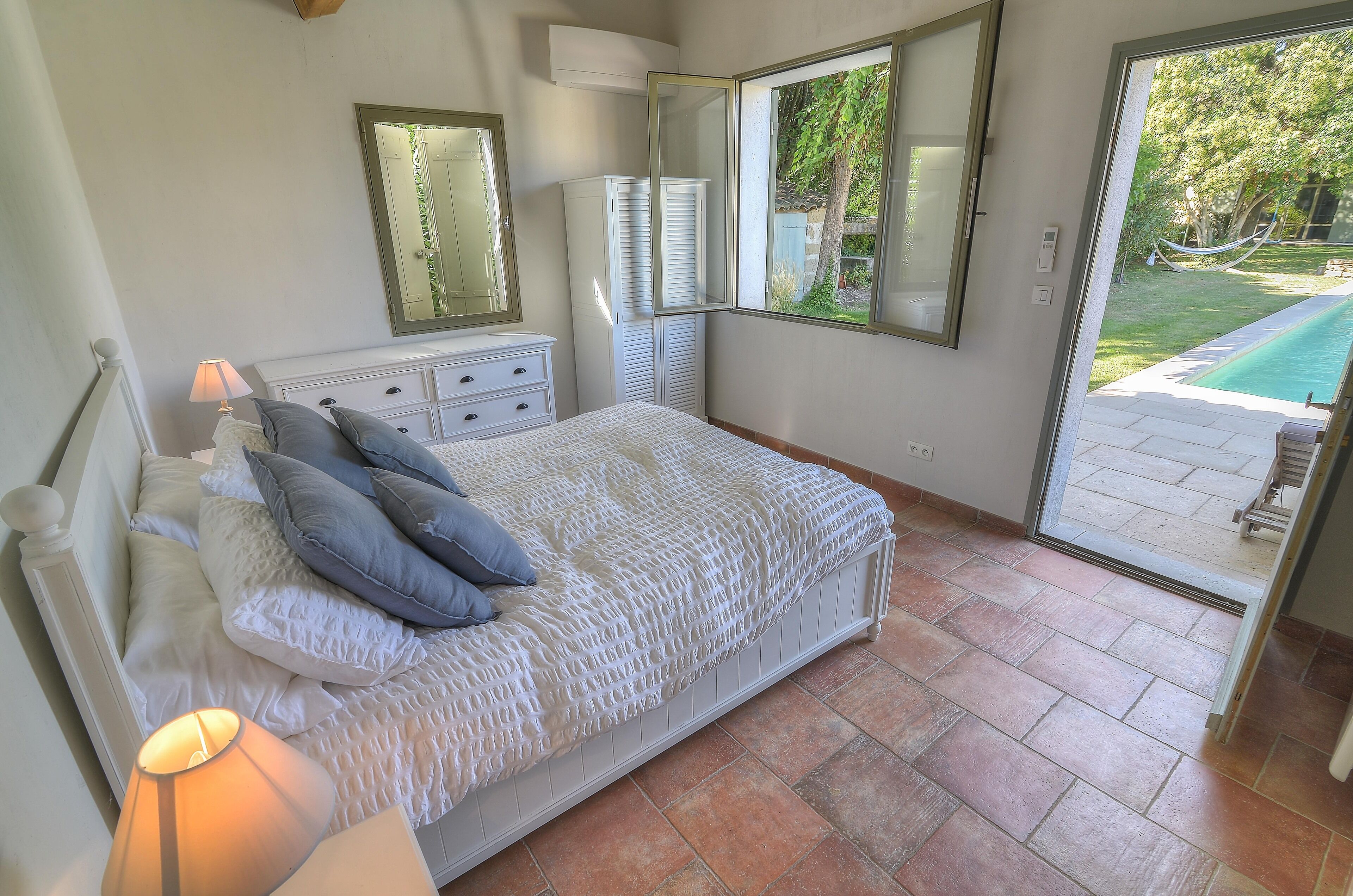 A bedroom with a bed, a dresser, a mirror, and a view of a swimming pool.