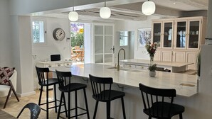 A modern kitchen with a large island, black bar stools, and pendant lighting.
