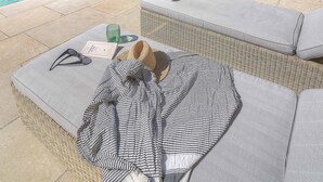 A poolside area with a wicker lounge chair, a towel, and a glass.