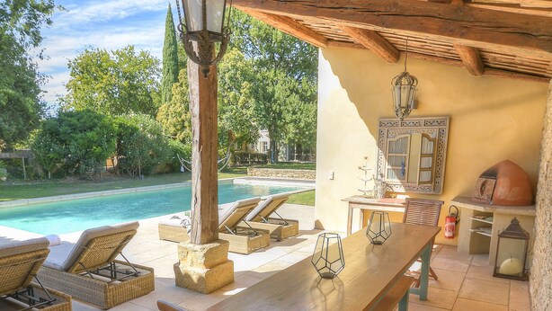 An outdoor patio with a pool, wooden furniture, and a stone table.