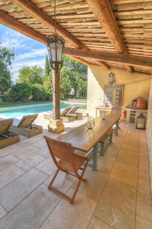 An outdoor patio with a pool, wooden furniture, and a stone table. - A stunning family home, 5 minutes from Uzes and 30 minutes from Avignon. (Saint-Quentin-La-Poterie)