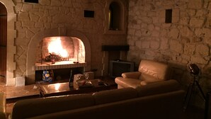 Habitación con paredes de piedra, chimenea, sofá de cuero y televisor.
