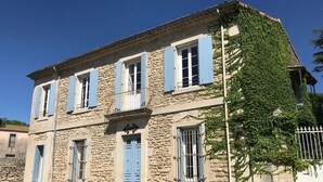 Un edificio de piedra con contraventanas azules, un balcón y una valla blanca.