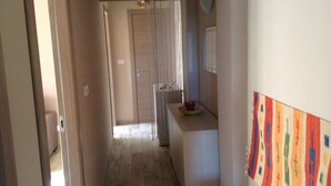 A narrow hallway with a wooden floor, a door at the end, and a small table with a bowl and plate.