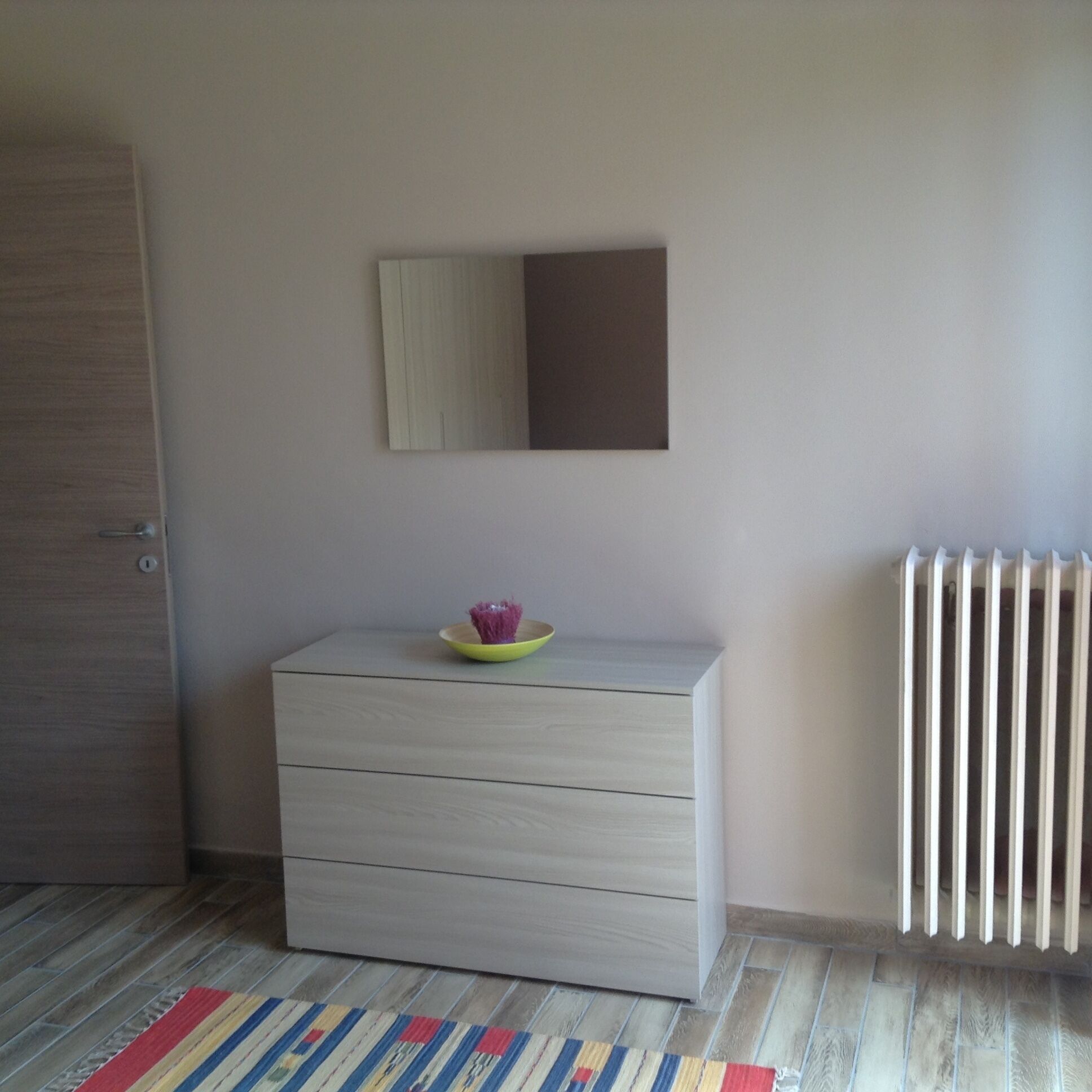 A room with a wooden dresser, a mirror, a radiator, and a striped rug.