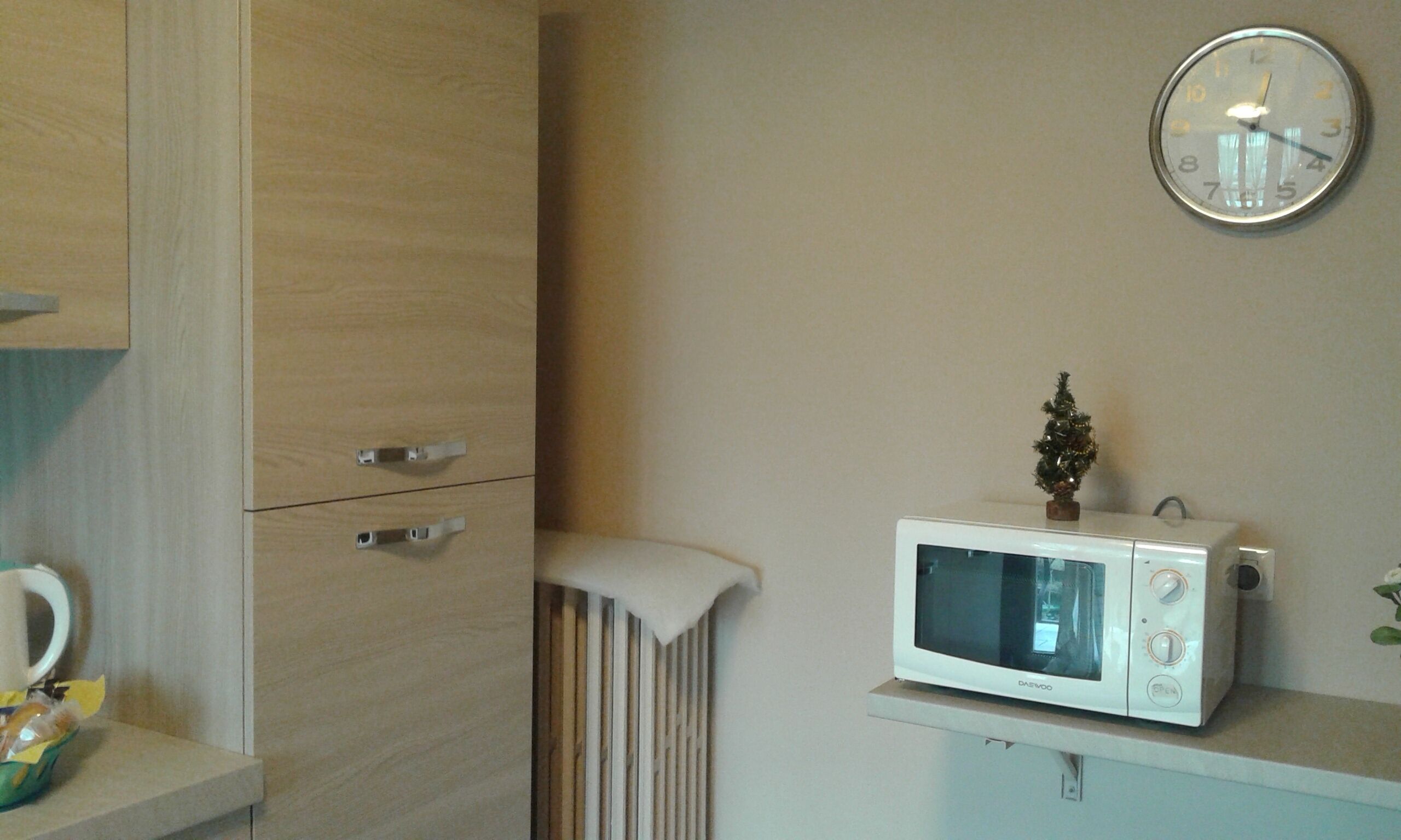 Una cocina con un microondas sobre la encimera, un pequeño árbol de Navidad y un armario de madera con cajones.