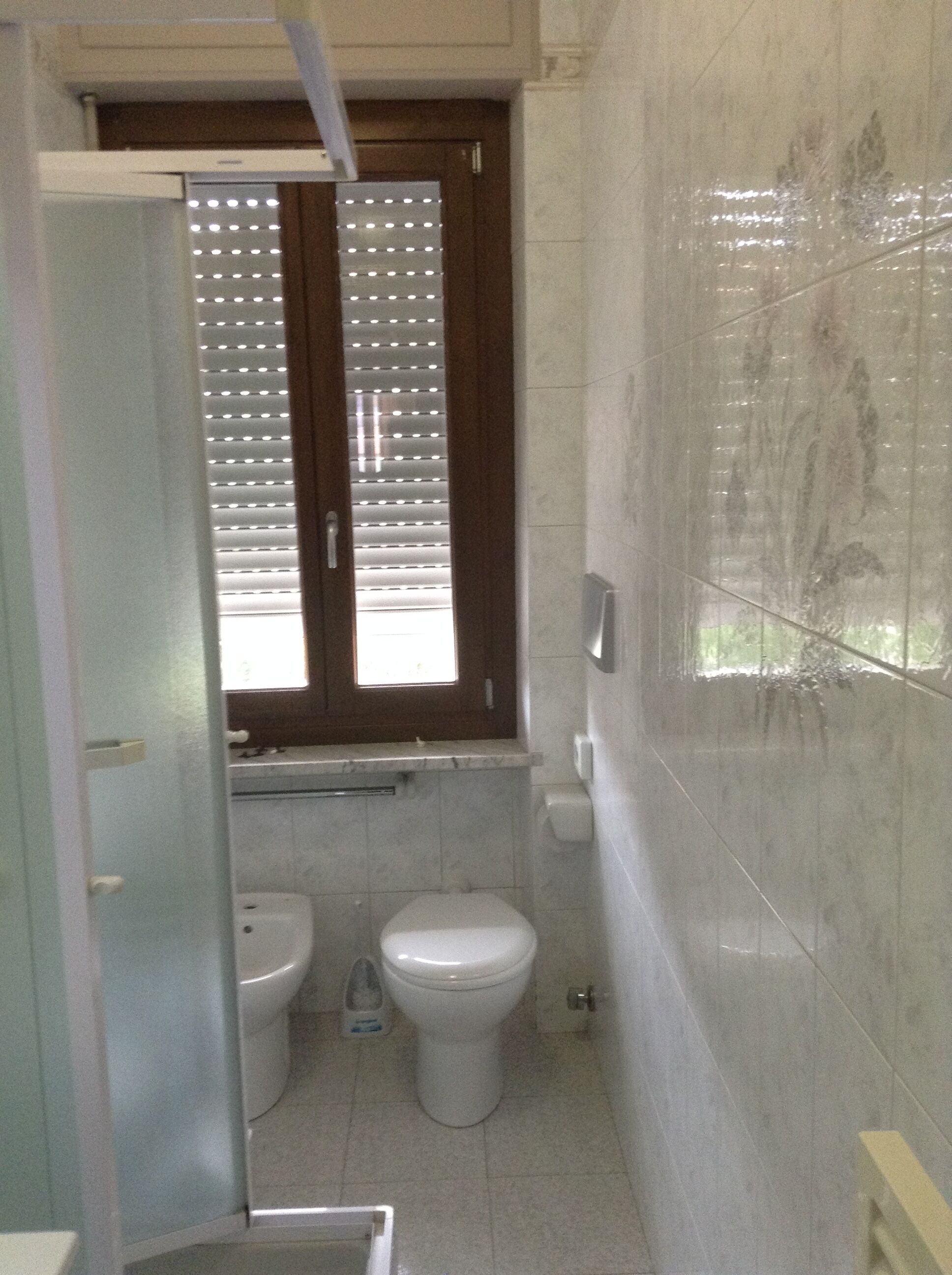 Une petite salle de bain comprenant des toilettes, un bidet et une fenêtre avec des stores.