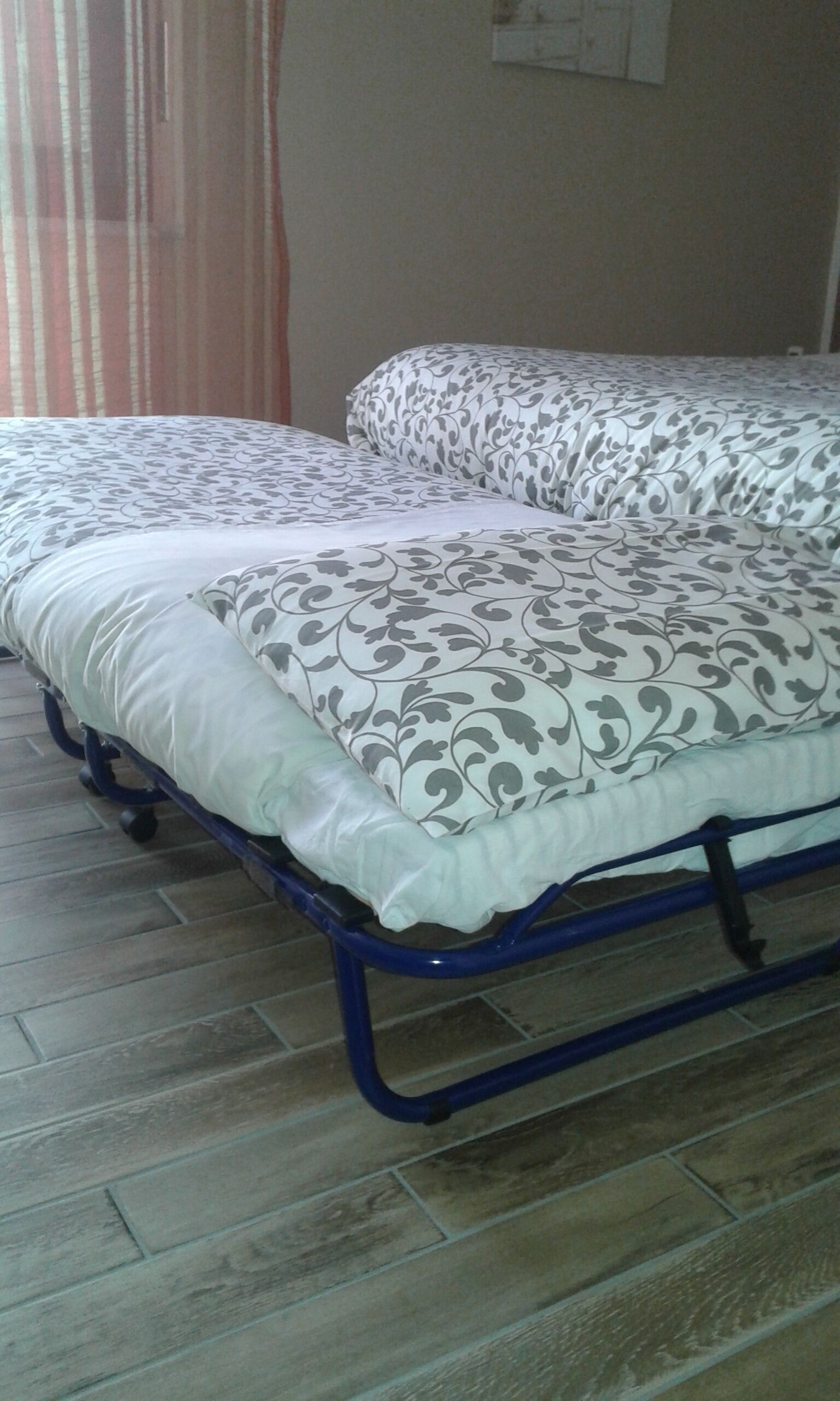 Un lit avec une couvre-lit à motifs et des oreillers, un cadre en métal bleu et un sol carrelé.