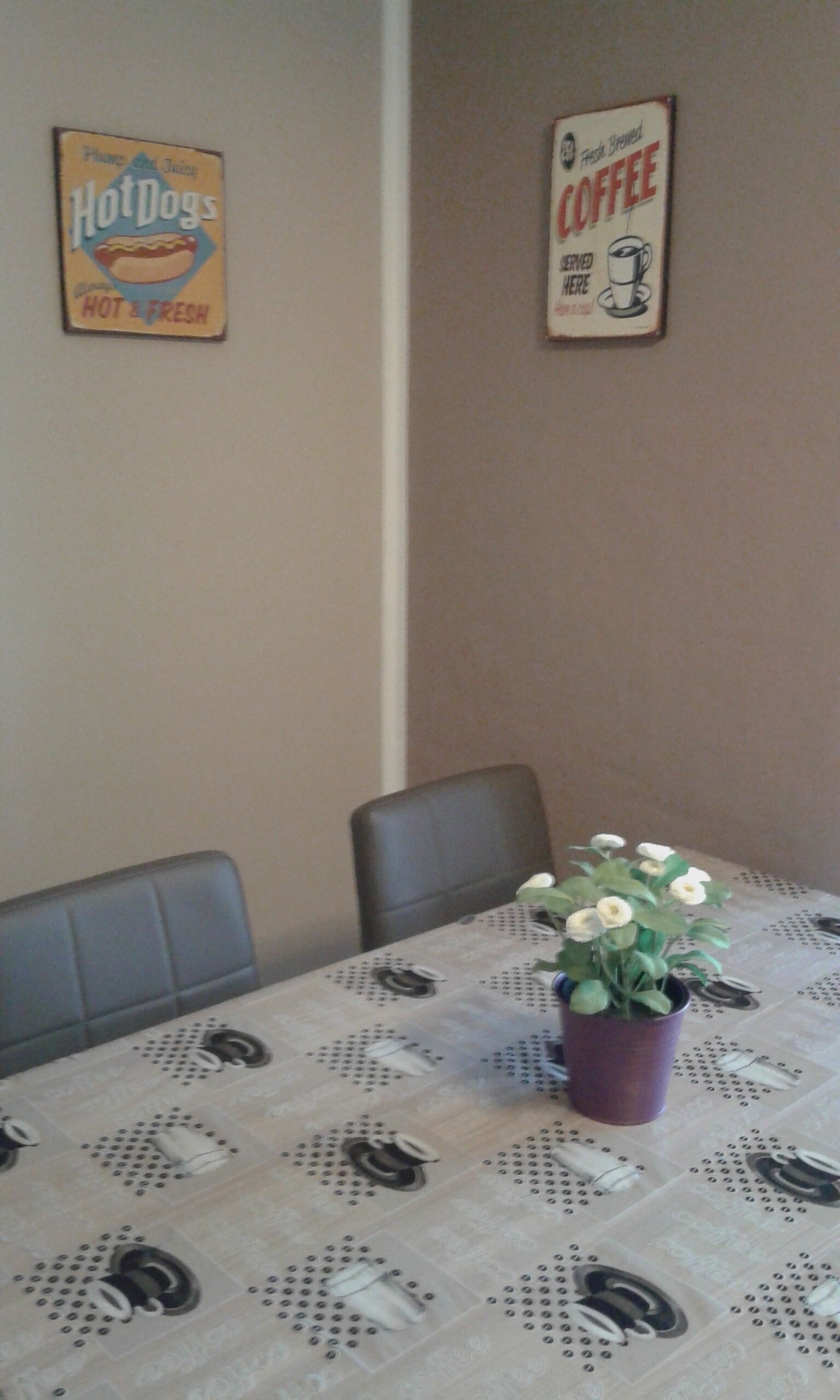 A dining area with a table covered by a tablecloth with a dotted pattern, two chairs, and a potted plant with white flowers.