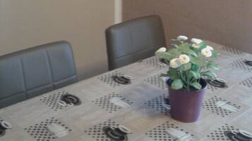 A dining area with a table covered by a tablecloth with a dotted pattern, two chairs, and a potted plant with white flowers.