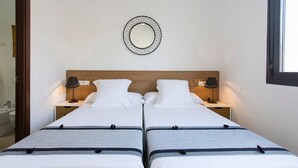 Ein Doppelzimmer mit zwei Betten, einem hölzernen Kopfteil, Nachttischlampen, einem Wandspiegel und einem Fenster.