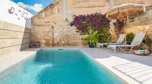 Une piscine bordée d’un muret en pierre, avec des chaises longues et des plantes en pot.