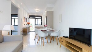 Ein modernes Wohnzimmer mit Flachbildfernseher, einer Couch und einem Essbereich mit Tisch für vier Personen.