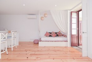 A room with a wooden floor, a white sofa with colorful pillows, a small table with chairs, and a door leading outside. - Oporto Vintage Apartment (Porto)