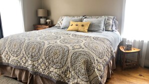 A bedroom with a large bed, a nightstand, a lamp, and a window with curtains.